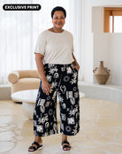 Woman wearing a white top and black patterned pants in a living room.