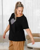 Woman wearing a black t-shirt with a silver heart design in a living room.