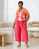 Woman wearing a colorful top and pink pants in a living room setting