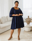 Woman in a navy blue dress standing in a living room.