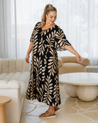 Woman in a black and beige patterned dress standing in a modern living room.