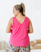 Woman wearing a bright pink tank top and floral pants in a room with white walls and beige furniture.