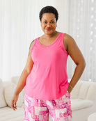 Woman wearing a pink tank top and patterned pants in a bright room.