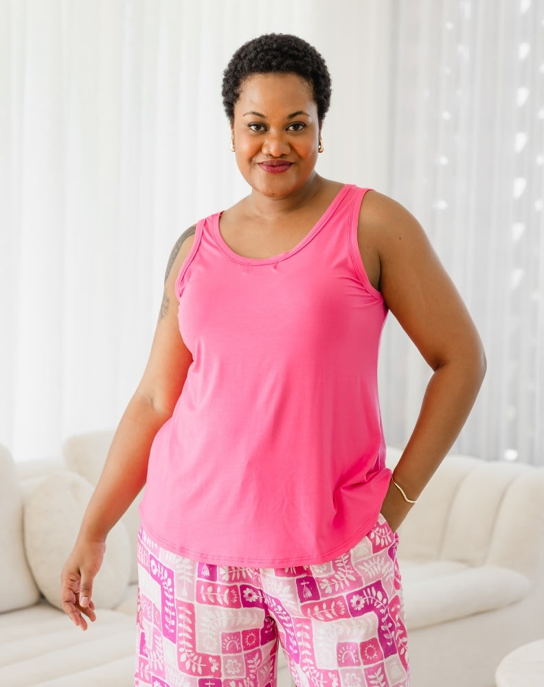 Woman wearing a pink tank top and patterned pants in a bright room.