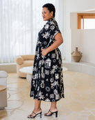Woman wearing a black dress with white floral patterns in a modern living room.