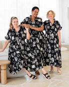 Three women wearing black and white patterned dresses in a living room setting.
