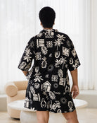 Person wearing a black shirt with white patterns in a room with white curtains and a beige chair.