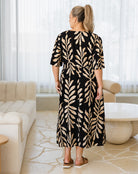 Woman wearing a black dress with beige leaf pattern in a modern living room.