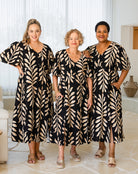 Three women wearing matching black and beige patterned dresses in a bright room.