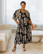 Woman wearing a black and beige leaf-patterned dress in a modern living room.