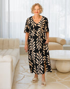Woman wearing a black dress with beige leaf pattern in a modern living room.