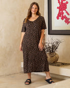 Woman wearing a leopard print dress standing in a room with a vase and artwork on the wall.