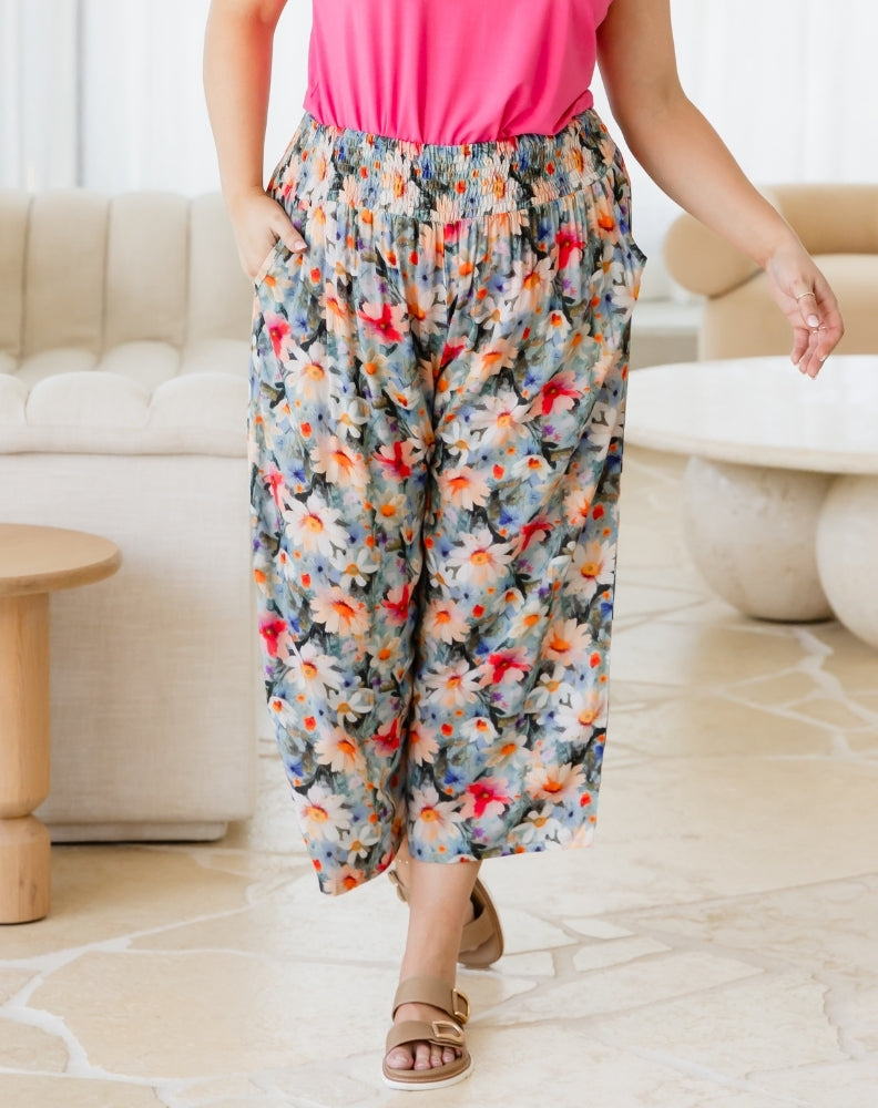 Person wearing colorful floral pants and a pink top in a living room setting.