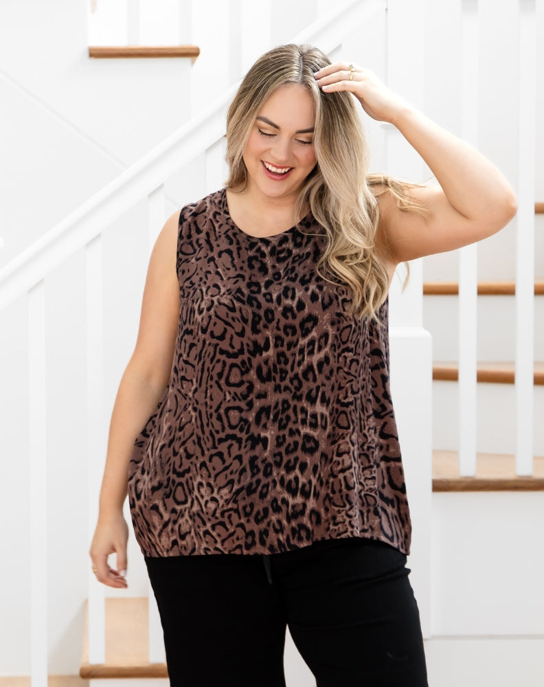 Woman wearing a leopard print sleeveless top and black pants in a home setting.