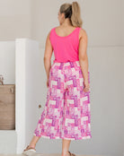 Woman wearing a pink sleeveless top and checkered pants against a neutral background