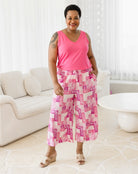 Woman wearing a pink sleeveless top and patterned pants in a living room.