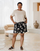 Woman wearing a white t-shirt and black floral shorts in a bright room.