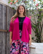 Woman wearing a bright pink cardigan over a black top with floral pants, standing outdoors.