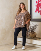 Woman wearing a leopard print top and black pants standing indoors.