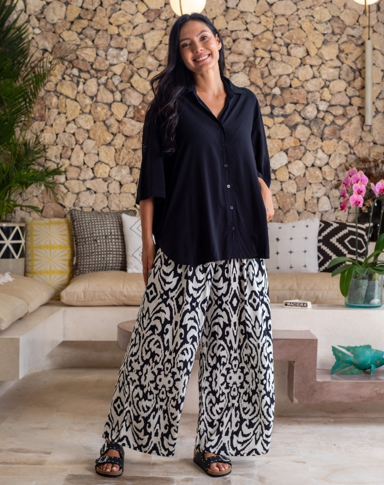 Woman wearing a black shirt and patterned pants standing in a room with stone walls and decorative elements.