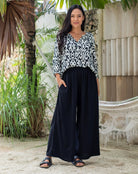 Woman wearing a black and white patterned top and black pants standing outdoors.