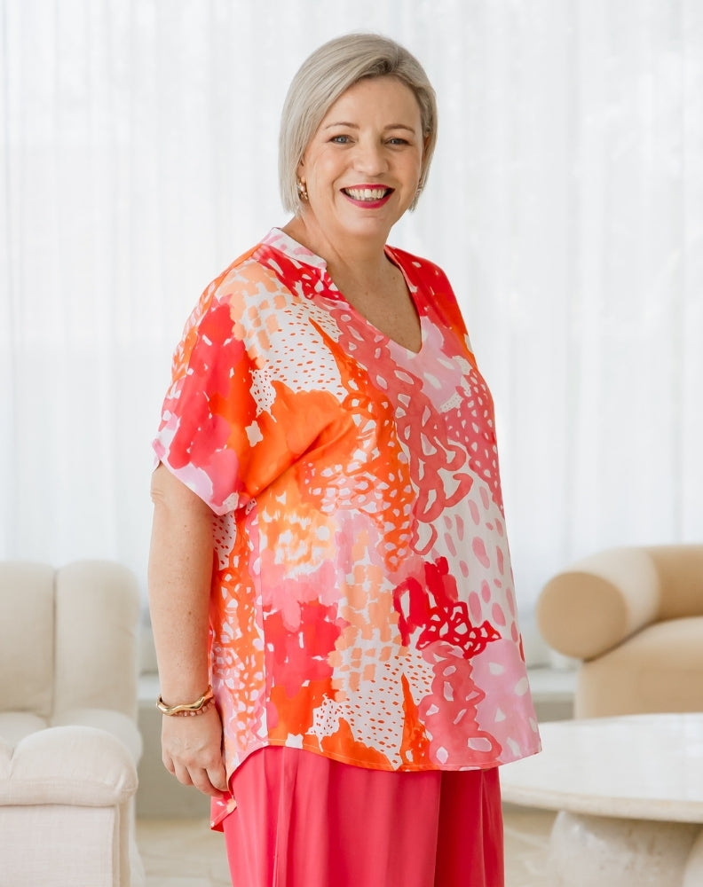Woman wearing a colorful floral blouse and pink pants in a living room setting