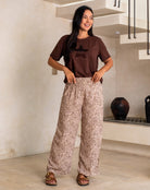 Woman wearing a brown t-shirt and patterned pants standing indoors.