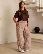 Woman wearing a brown top and patterned pants standing in a room with a staircase.