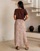 Woman in a brown top and patterned skirt standing in a room with a staircase.