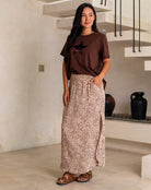 Woman wearing a brown t-shirt and patterned skirt standing in a modern indoor setting.