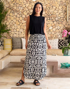 Woman wearing a black sleeveless top and patterned skirt standing in a living room.