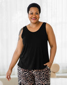 Woman wearing a black tank top and leopard print pants against a white curtain background