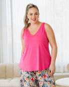 Woman wearing a bright pink tank top and floral pants indoors.