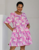 Woman wearing a pink and white patterned dress against a plain background
