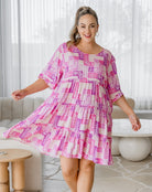 Woman wearing a pink and white patterned dress in a living room setting