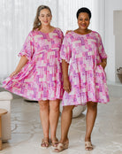 Two women wearing pink and white patterned dresses in a bright room.