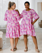 Two women wearing matching pink and white patterned dresses in a room.