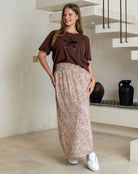 Woman wearing a brown top and patterned pants standing in a modern indoor setting.