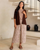 Woman wearing a brown top and patterned pants standing in a modern indoor setting.