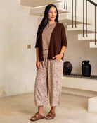 Woman wearing a brown cardigan, beige top, and leopard print pants in a modern indoor setting.