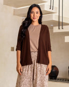 Woman wearing a brown cardigan over a beige top and leopard print pants in an indoor setting.