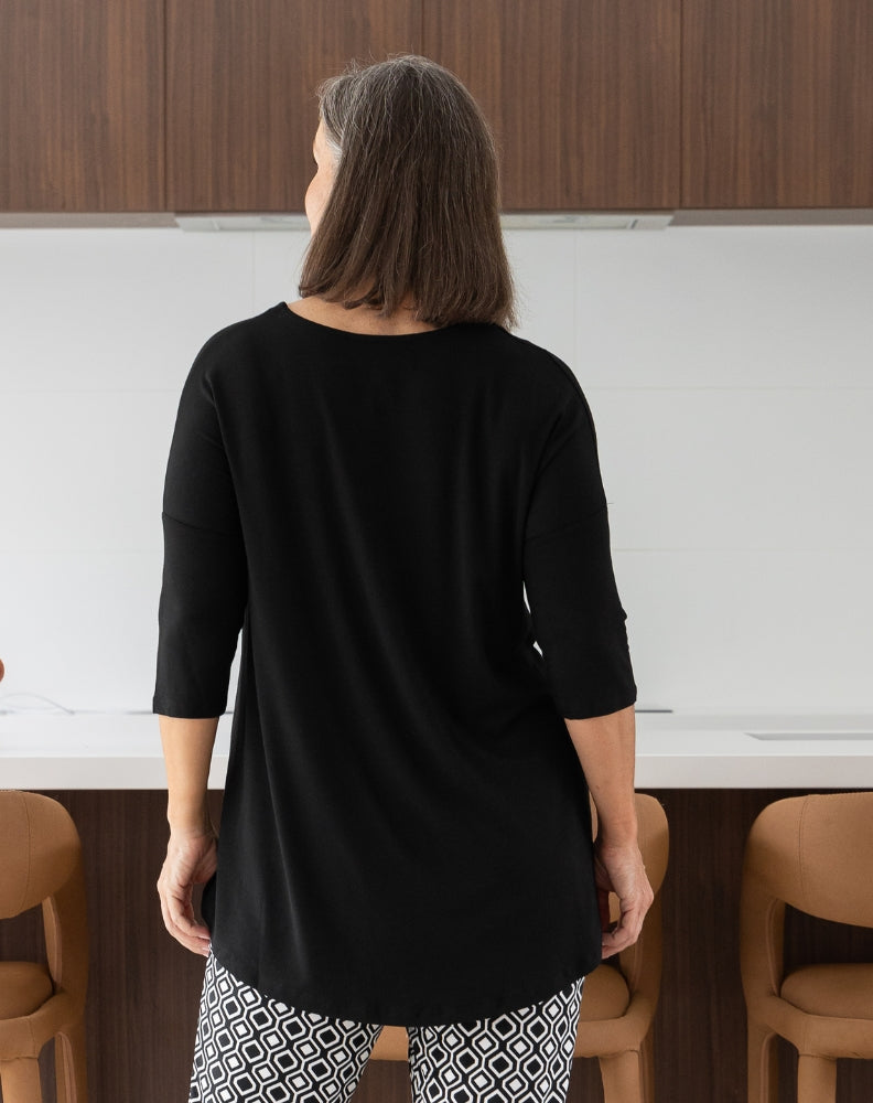 Person wearing a black top and patterned pants in a kitchen setting
