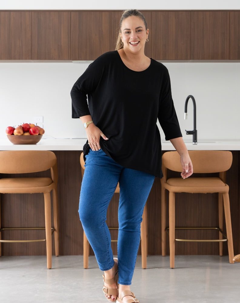 Woman standing in a kitchen wearing a black top and blue jeans.