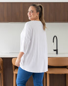 Woman standing in a kitchen wearing a white shirt and blue pants.