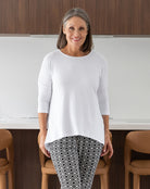 Woman wearing a white top and patterned pants standing in a kitchen.