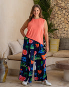 Woman wearing a bright orange sleeveless top and colorful patterned pants in a living room setting.
