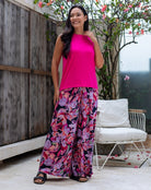 Woman wearing a bright pink top and floral pants standing outdoors.