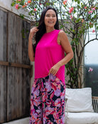 Woman wearing a bright pink top and floral pants standing outdoors.