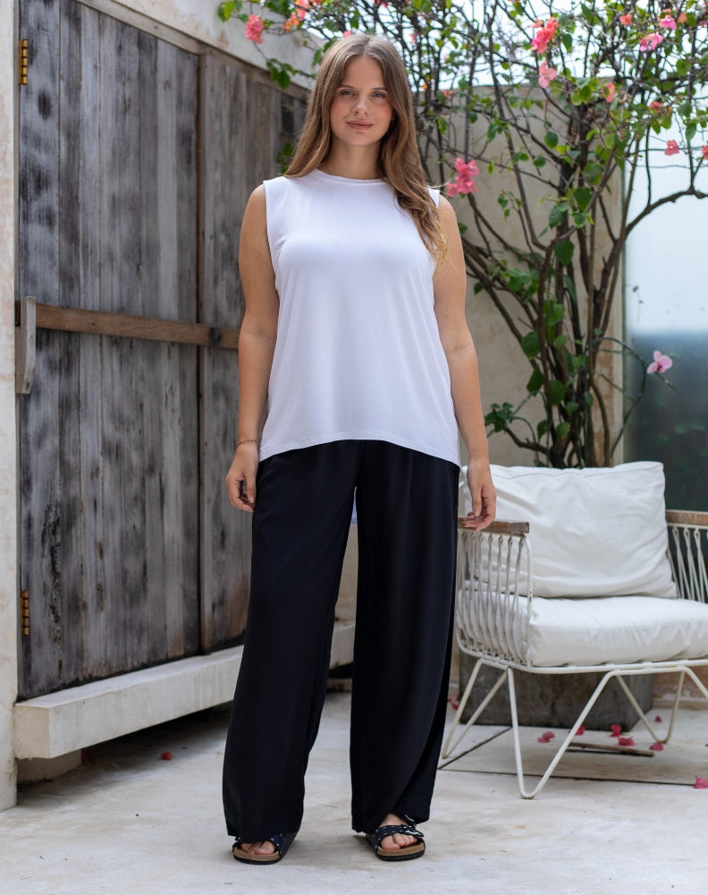 Woman wearing a white sleeveless top and black pants standing outdoors.