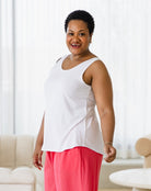 Woman wearing a white top and pink pants in a bright room with white curtains.